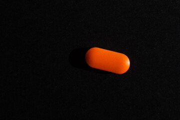 Single orange pill on black background with shadow