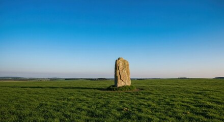 Standing stone in a green field under a clear blue sky, rural landscape