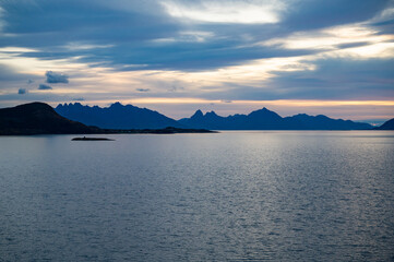 A serene seascape at dawn features a calm body of water with distant mountains and a solitary island, under a soft, colorful sky, Sortland, Norway