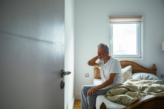 Senior man experiencing neck pain in bedroom - Powered by Adobe