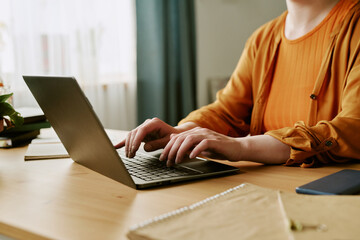 Caucasian young adult woman sitting at desk typing on laptop, hands and upper body visible, showing partial hair loss on scalp, concept of alopecia and remote work