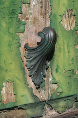 Dettaglio di una maniglia in bronzo su una porta di legno dipinta di verde con la vernice scrostata