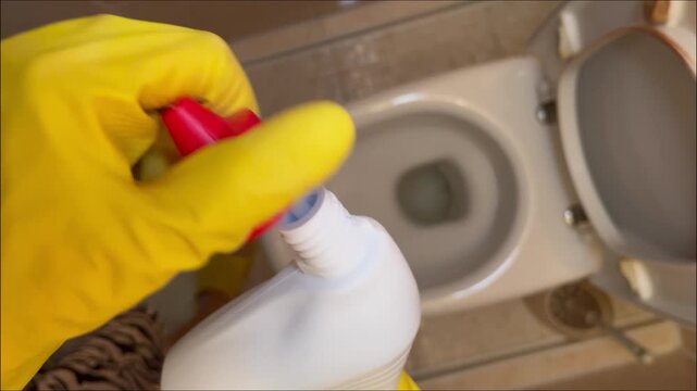 Close-up of gloved hand gripping cleaning bottle, preparing to apply solution to toilet, showcasing cleaning action with gradual camera zoom emphasizing the task