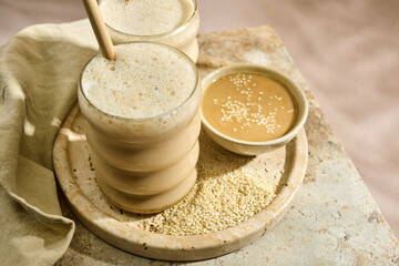Sesame Tahini Latte Delight. Creamy sesame paste and iced tahini lattes on rustic travertine surface.