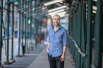 Fototapeta premium Hispanic Man Standing Confidently Under Urban Manhattan NYC Scaffolded Walkway with Blurred Background
