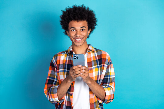 Young man smiles while using smartphone in colorful plaid shirt against a bright blue background for lifestyle advertising - Powered by Adobe