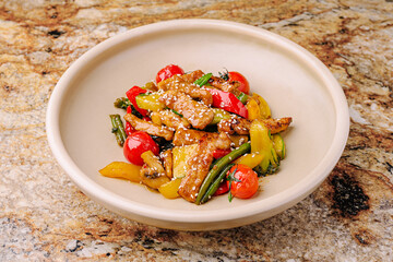 Colorful stir-fried vegetables with chicken served in a bowl on a stone surface
