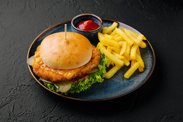 Crispy chicken burger served with golden fries and ketchup on a black plate