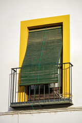 Sunlit window balcony with a green bamboo blind framed by yellow, reflecting Andalusian charm, simple architecture, and the warmth of daily life under the southern Spanish light