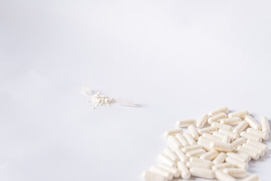Many white capsules with lactobacilli and one open capsule on a white background.