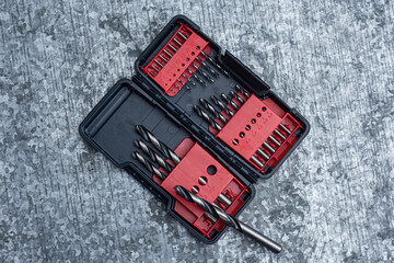 Drill bit set in a plastic case on a textured metal workbench. Concept for DIY, construction and repair projects.