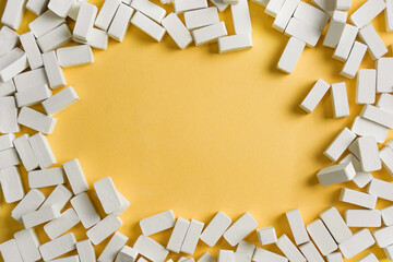 Top view of white miniature bricks scattered to form a frame with empty center on yellow background. Creative abstract composition.