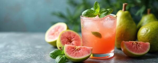 Glass of pink guava drink with ice and mint garnish. Ripe guavas and mint sprigs surround the beverage on a textured surface. Refreshing summer refreshment.