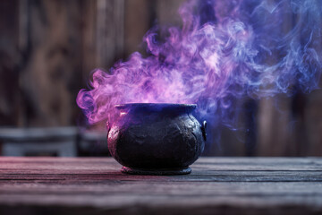 Mysterious ancient black cauldron emitting swirling purple and blue smoke on weathered wooden surface with blurred rustic background providing magical atmosphere