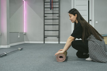 Asian woman is rolling yoga mat in sport studio, close-up.