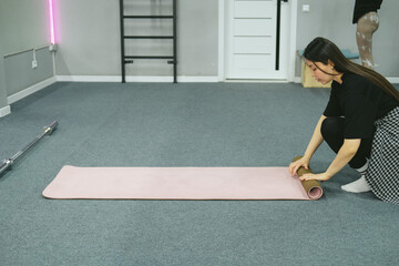 Asian woman is rolling yoga mat in sport studio, close-up.