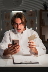 Credit card fraud. phone scam. Male doctor man shocked financial theft while working on night...