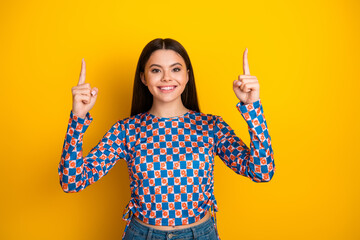 Bright smiling young woman wears a blue and orange checkered top against a vivid yellow background...