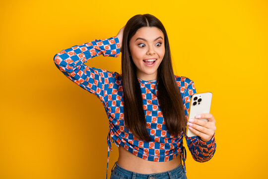 Fototapeta Happy young girl with long brunette hair takes a selfie on a bright yellow background wearing a patterned blue and orange top and casual jeans