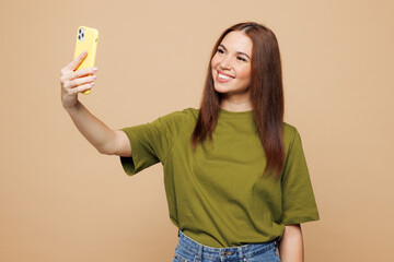 Young smiling happy woman she wears green t-shirt casual clothes doing selfie shot on mobile cell phone post photo on social network isolated on plain pastel light beige background. Lifestyle concept.