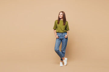 Full body young smiling happy woman she wear olive green t-shirt casual clothes stand look aside on blank empty area isolated on plain pastel light beige background studio portrait. Lifestyle concept © ViDi Studio