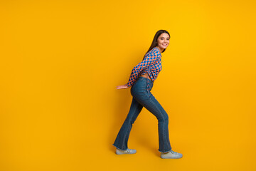 Young woman in jeans and colorful top walks with a smile against a bright yellow background