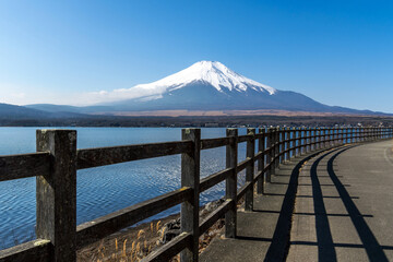 Scenic walkway by the lake with clear view of snow-capped Mount Fuji under blue sky. Perfect for travel, landscape, Japan tourism, wellness, and nature lifestyle design concepts.