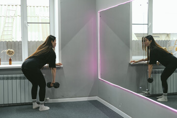 Strong beautiful fitness asian woman training, doing exercise with dumbbells at gym. Female sport athlete coach making workout bodybuilding on bench heavy fit equipment.