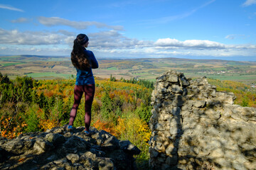 Fototapeta premium Young woman standing on Střílky Castle ruins overlooking autumn landscape in Chřiby, Czech Republic