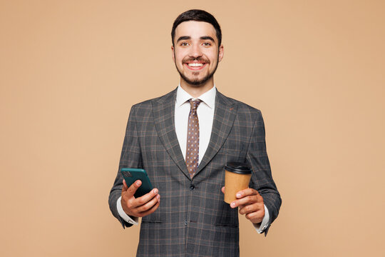 Young happy successful employee business man corporate lawyer wear classic formal grey suit shirt tie work in office hold use mobile cell phone drink coffee isolated on plain beige background studio - Powered by Adobe