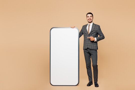Full body young employee business man corporate lawyer in classic formal grey suit shirt tie work in office point finger on big huge blank screen mobile cell phone isolated on plain beige background - Powered by Adobe