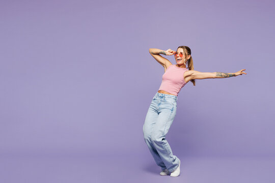 Full body side view young woman she wear pink tank top casual clothes sunglasses stand on toes lean back look aside isolated on plain pastel light purple background studio portrait. Lifestyle concept.