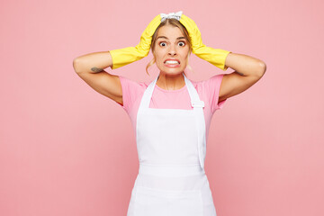 Young shocked surprised woman wear white apron rubber gloves doing housework tidy up look camera out hands on head isolated on plain pastel light pink background studio portrait. Housekeeping concept.