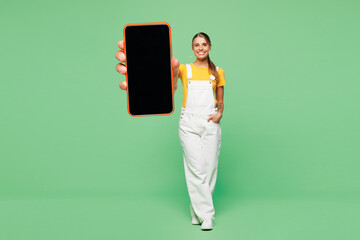 Full body young woman she wear yellow t-shirt overall casual clothes hold in hand use blank screen...