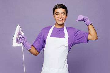 Young smiling happy husband man wear violet t-shirt hold iron show muscles on hand while doing housework tidy up isolated on plain pastel light purple background studio portrait. Housekeeping concept.