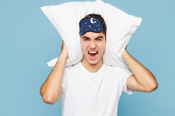 Calm young sad mad man he wear pyjamas jam sleep eye mask rest relax at home cover ears from neighbours noise snoring isolated on plain pastel light blue cyan background. Bad mood night nap concept.