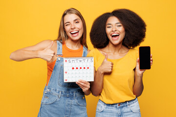 Two young friends buddies women in denim casual clothes together hold female periods calendar for...