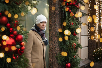 Adult man leaves luxury store decorated light garlands. Festive Christmas decorations. Xmas...