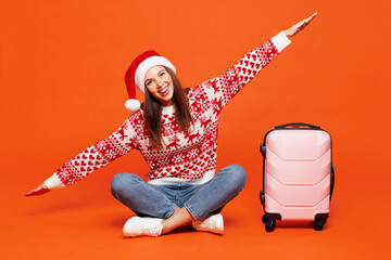 Traveler woman wear red Santa hat hold bag spread hands pov plane isolated on plain orange...
