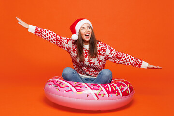 Traveler woman wear red Santa hat sit on rubber swim ring isolated on plain orange background...