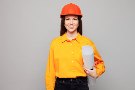 Young smiling happy architect engineer designer employee white woman wear yellow clothes hardhat hold blueprints isolated on plain pastel grey background studio portrait. People work on build project.