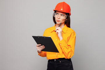 Young architect engineer designer employee white woman wears yellow clothes hardhat glasses hold clipboard sign paper account documents isolated on plain grey background. People work on build project.