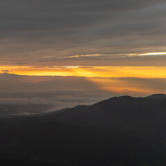 Sunrise over mountain peak with warm orange sky and peaceful clouds, morning light in Thailand highland, beautiful tropical landscape nature background.