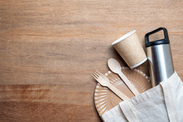 Eco-friendly flat lay with cotton tote bag, bamboo cutlery, paper cup, stainless bottle, and plate...