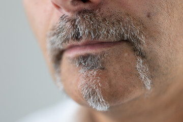 Extreme close-up of a man’s face focusing on his gray mustache and goatee. The detailed macro shot highlights the texture of facial hair and skin, captured in soft lighting.