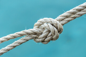Close-up of a strong rope knot with blue water background, symbolizing connection, strength, security, and teamwork. Ideal for conceptual use in business, safety, or maritime themes.