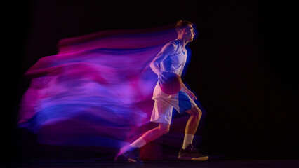 Basketball player dribbling ball in blue and purple motion light on dark background. Concept of brand identity, sport marketing, energy training, and expressive movement style.