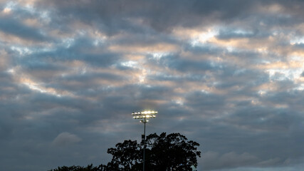 Sports field floodlights at dusk beneath dramatic layered clouds