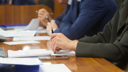 Business people and officials in suits sitting at desk, reviewing and signing documents with pens...
