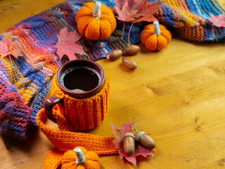 Colorful autumn composition, a mug of hot coffee in a knitted cover on a wooden table. Knitted small pumpkins and a scarf. Copy space